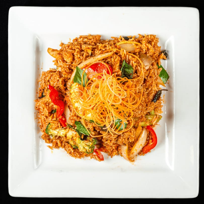 Thai Chilli Pepper's spicy fried rice with vegetables, chicken, and shredded carrots on a white plate.