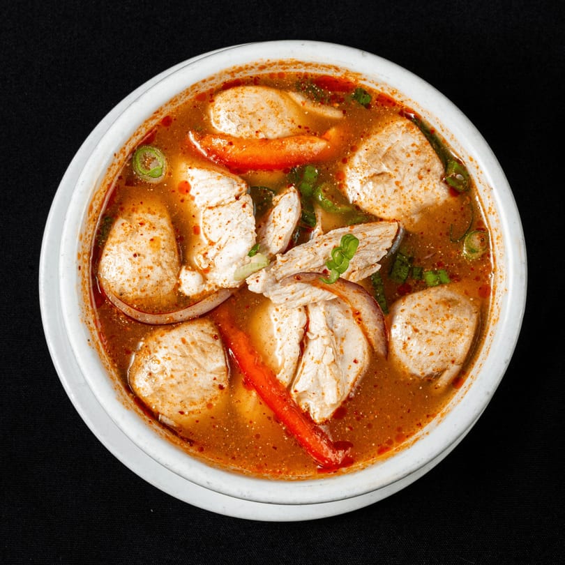Spicy Thai Tom Yum soup with chicken, red peppers, and green onions in a white bowl.