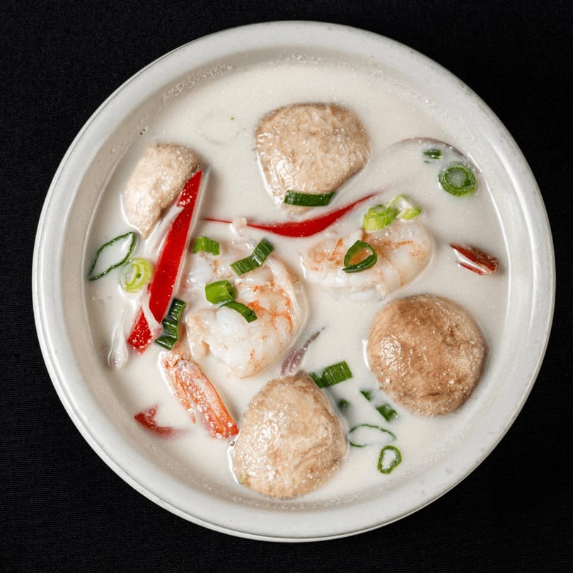 Creamy Thai soup with shrimp, mushrooms, red peppers, and green onions in a white bowl.