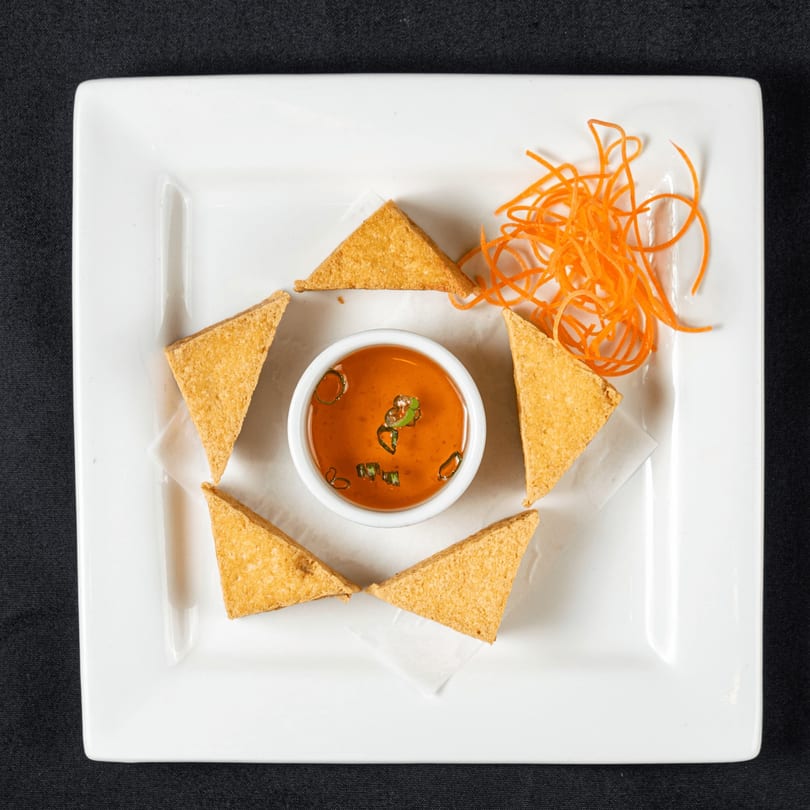 Golden fried tofu triangles arranged around a small bowl of dipping sauce with shredded carrots.